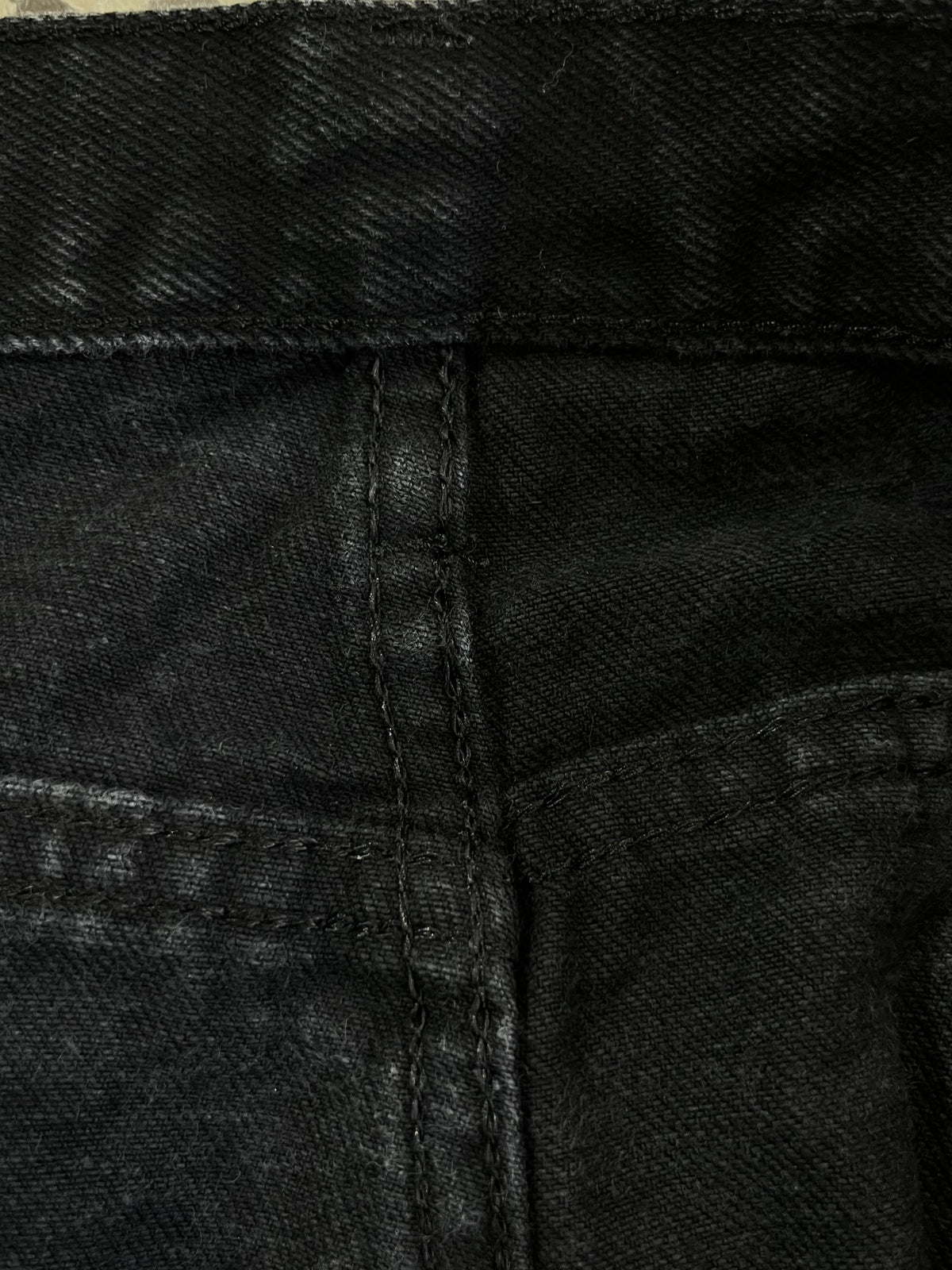 Close-up of black denim fabric showing the waistband, center seam, and pocket stitching.