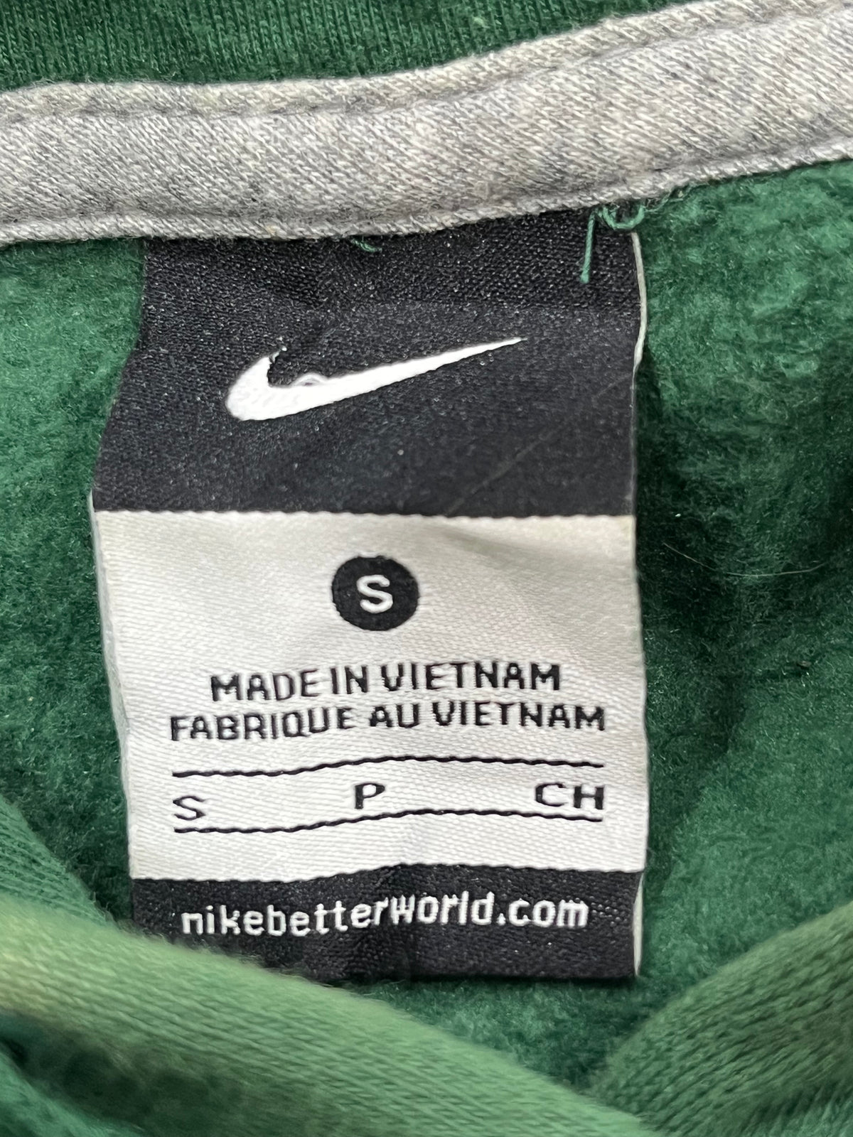 Close-up of a Nike garment label inside a green fleece or sweatshirt, showing the white Nike swoosh, size S, and the website nikebetterworld.com.