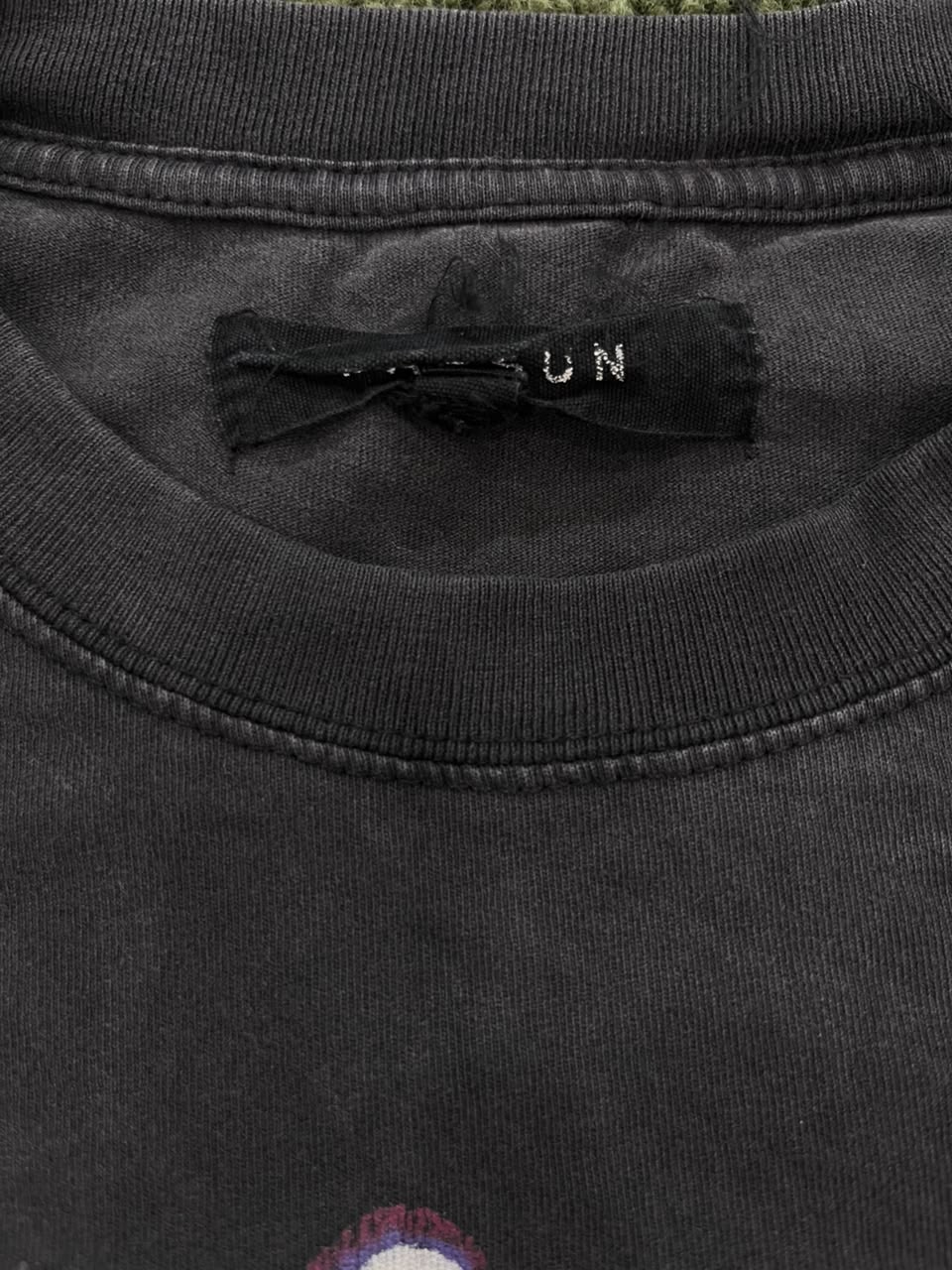 Close-up of a washed black crewneck t-shirt showing the inner neck label with 'UN' embroidered on it.