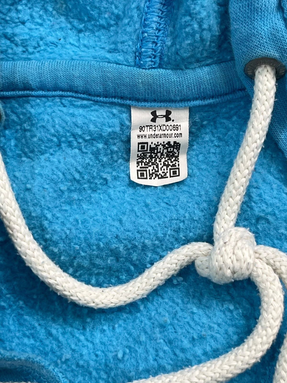 Close-up of a bright blue fleece hoodie showing the white drawstrings and a sewn-on Under Armour brand tag.