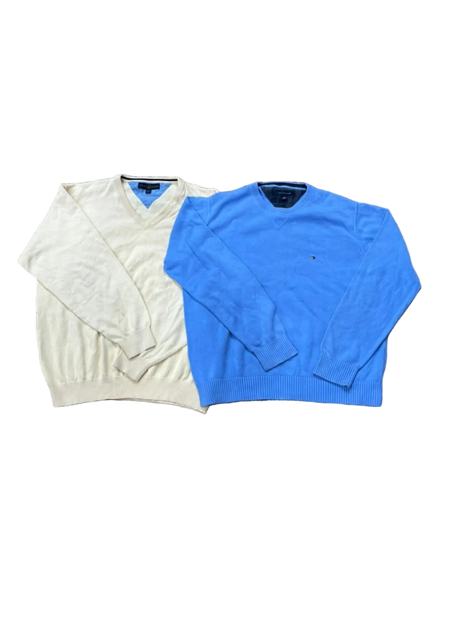 Two long-sleeve knit V-neck sweaters laid flat on a brown shag rug: one pale cream and one bright blue. Bare feet are visible at the bottom edge.