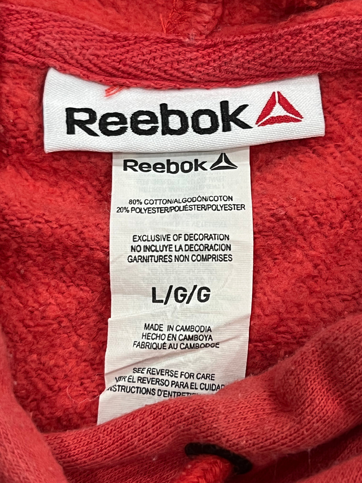 Close-up of a red knit garment showing the Reebok brand label sewn inside the collar, with the white Reebok logo and red triangle visible on the fabric tag.