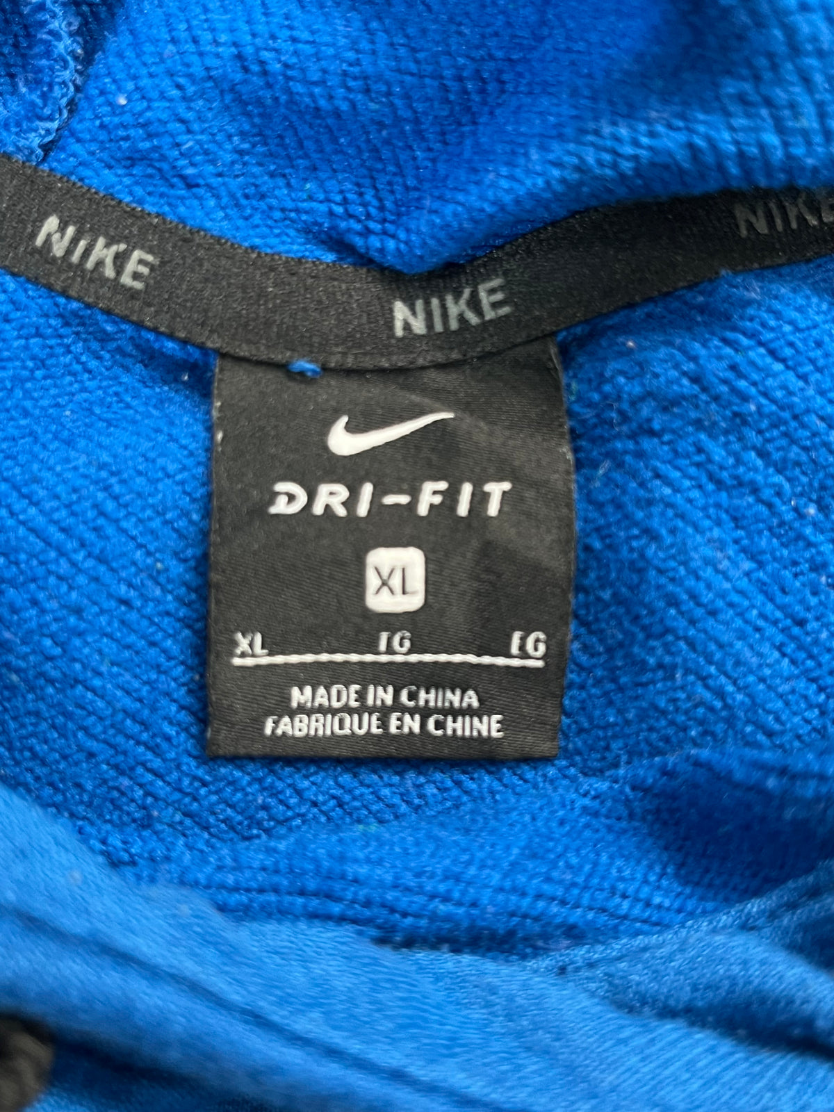 Close-up of a Nike Dri-Fit garment label inside a bright blue ribbed fabric, showing the Nike swoosh, Dri-Fit branding, and size XL.