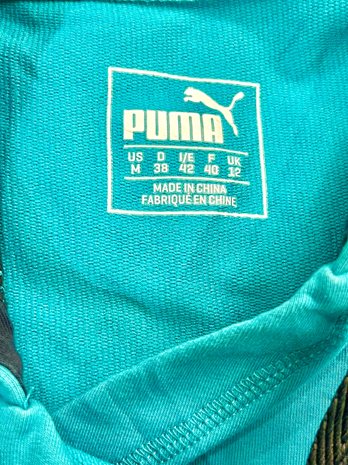 Close-up of a turquoise blue Puma garment showing the inner neck label with white Puma branding and size information.