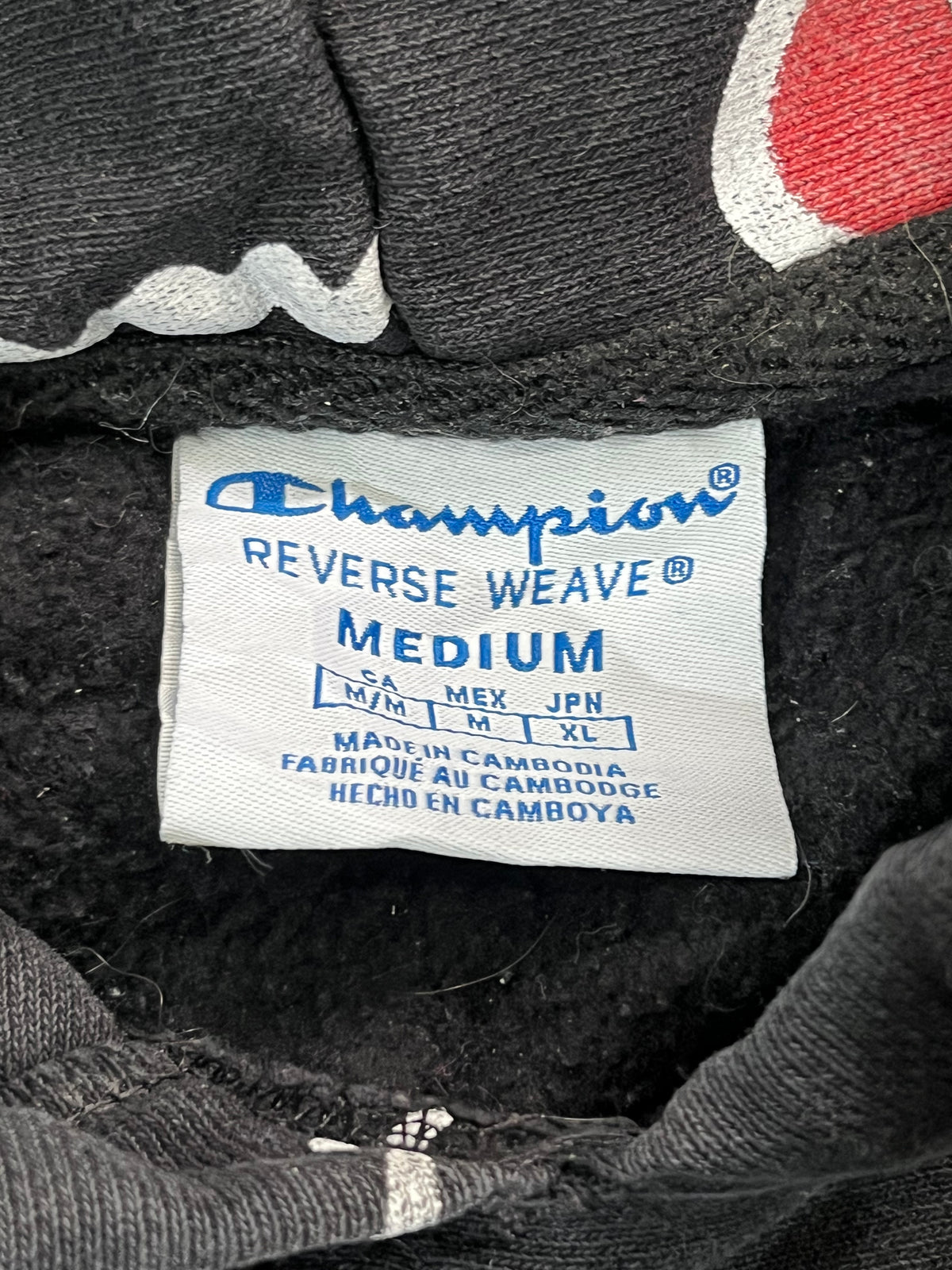 Close-up of a Champion garment interior label reading REVERSE WEAVE MEDIUM, shown sewn into dark charcoal fabric.