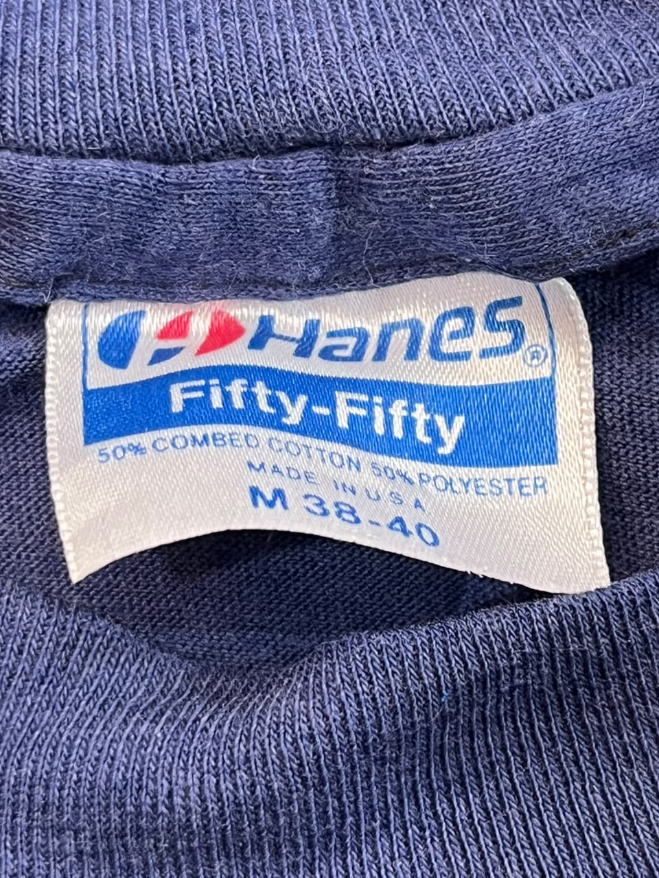 Close-up of a Hanes Fifty-Fifty garment label sewn inside the collar of a blue ribbed knit top, showing the brand name and fabric composition.