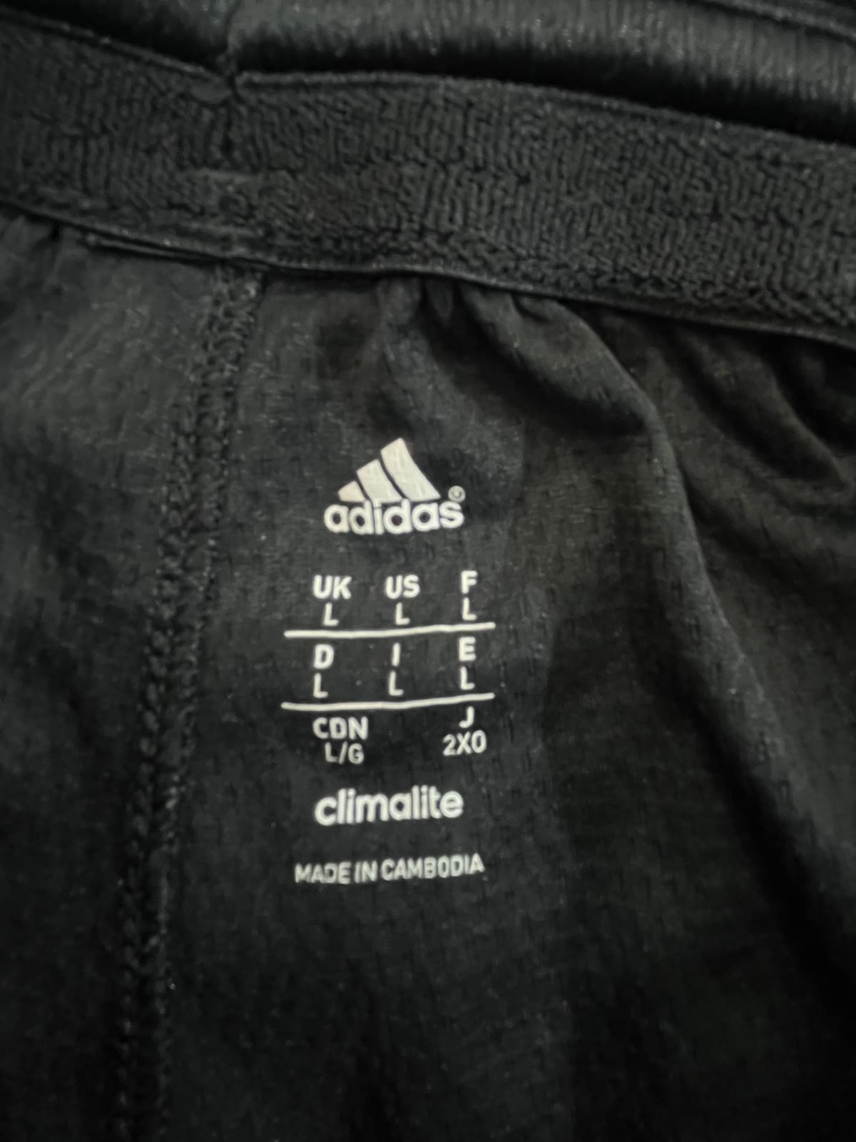 Close-up of the inner label of black Adidas sportswear, showing the Adidas logo, size conversion chart, Climalite technology, and Made in Cambodia text.
