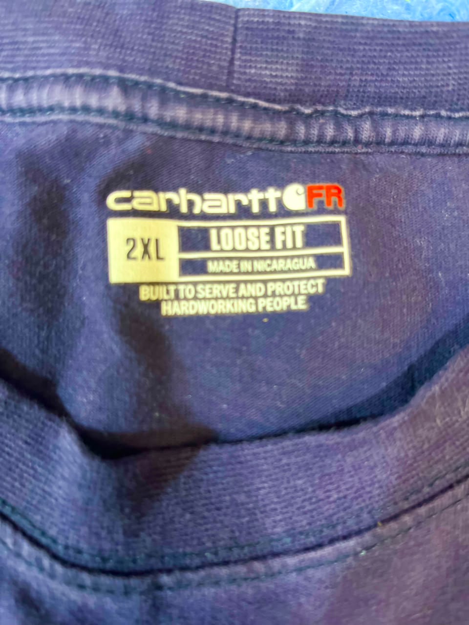 Close-up of a Carhartt FR size 2XL loose fit garment label sewn inside the collar of a dark navy blue shirt.