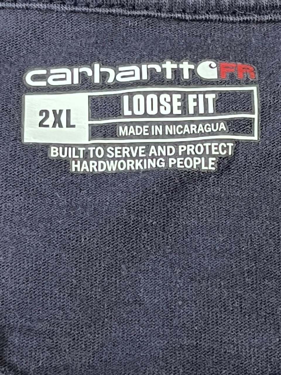 Close-up of a Carhartt FR 2XL Loose Fit garment label sewn onto dark charcoal gray fabric.