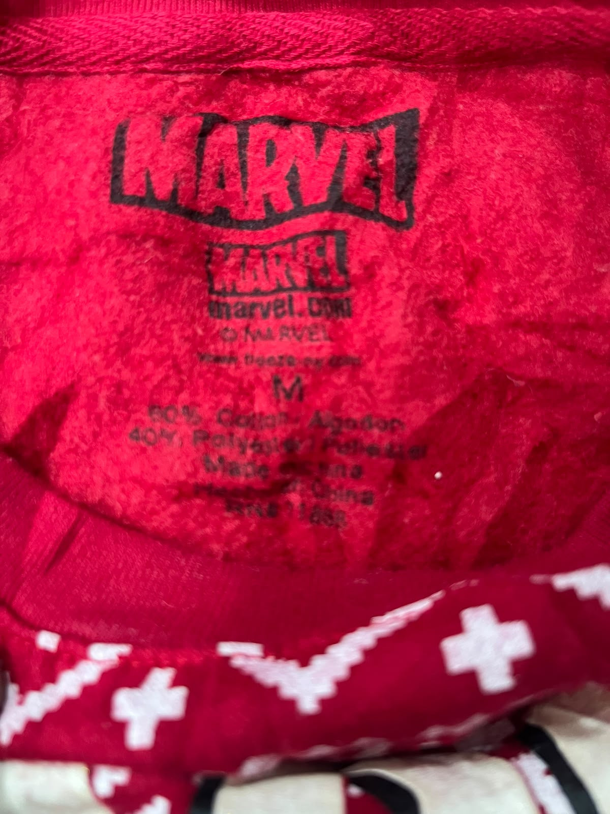 Close-up of a red plush fabric item with a black Marvel logo printed on the front and size/manufacturer text inside.