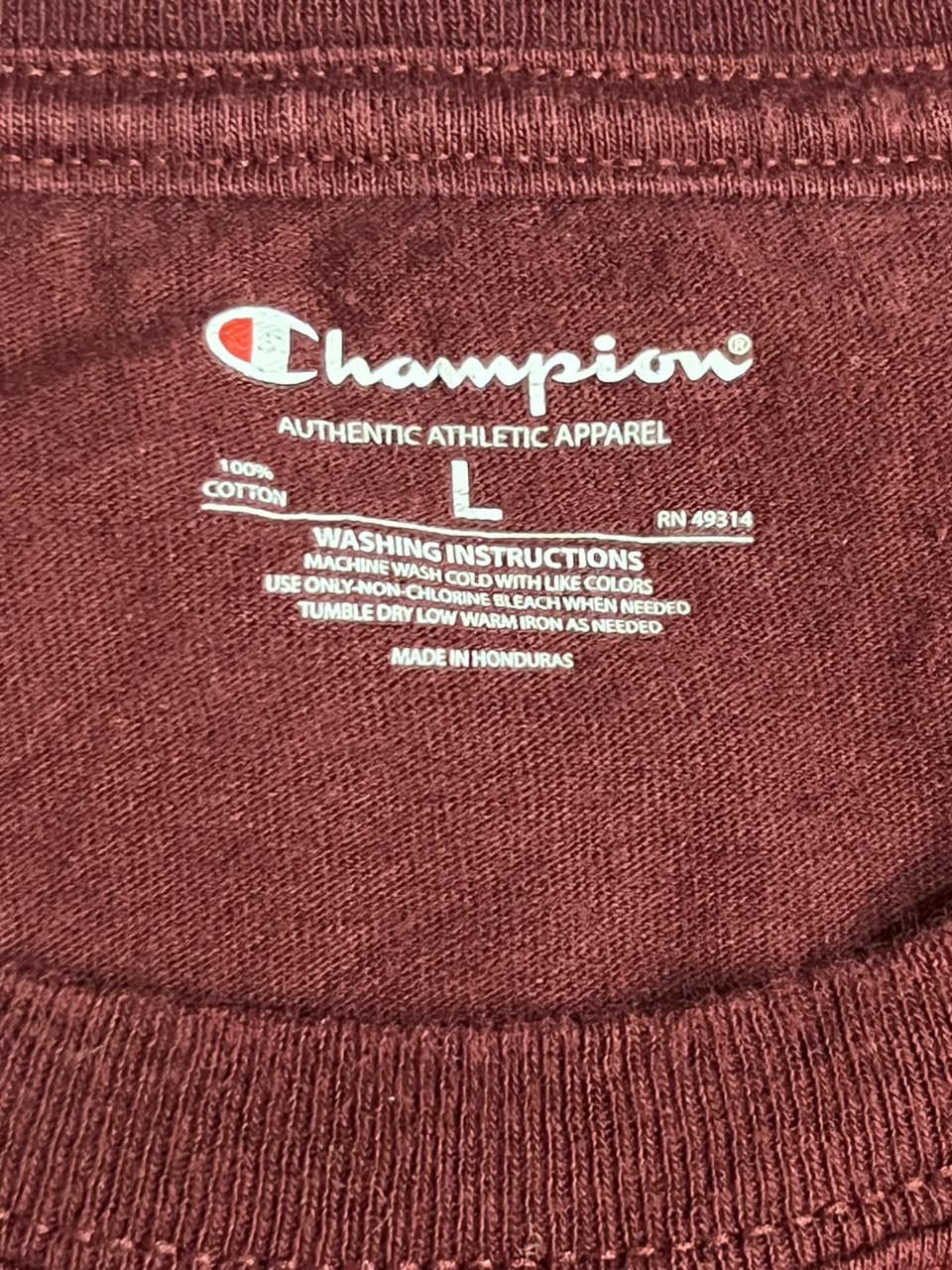 Close-up of a Champion athletic apparel garment neck label, showing the white Champion logo and text on a burgundy ribbed fabric background.