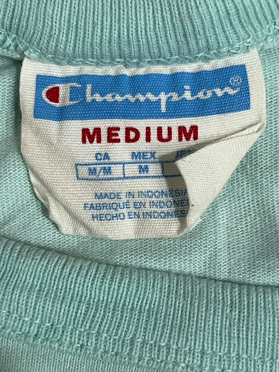 Close-up of a Champion sweater neck label reading MEDIUM, with the blue and white Champion logo and size information visible on the knit fabric.