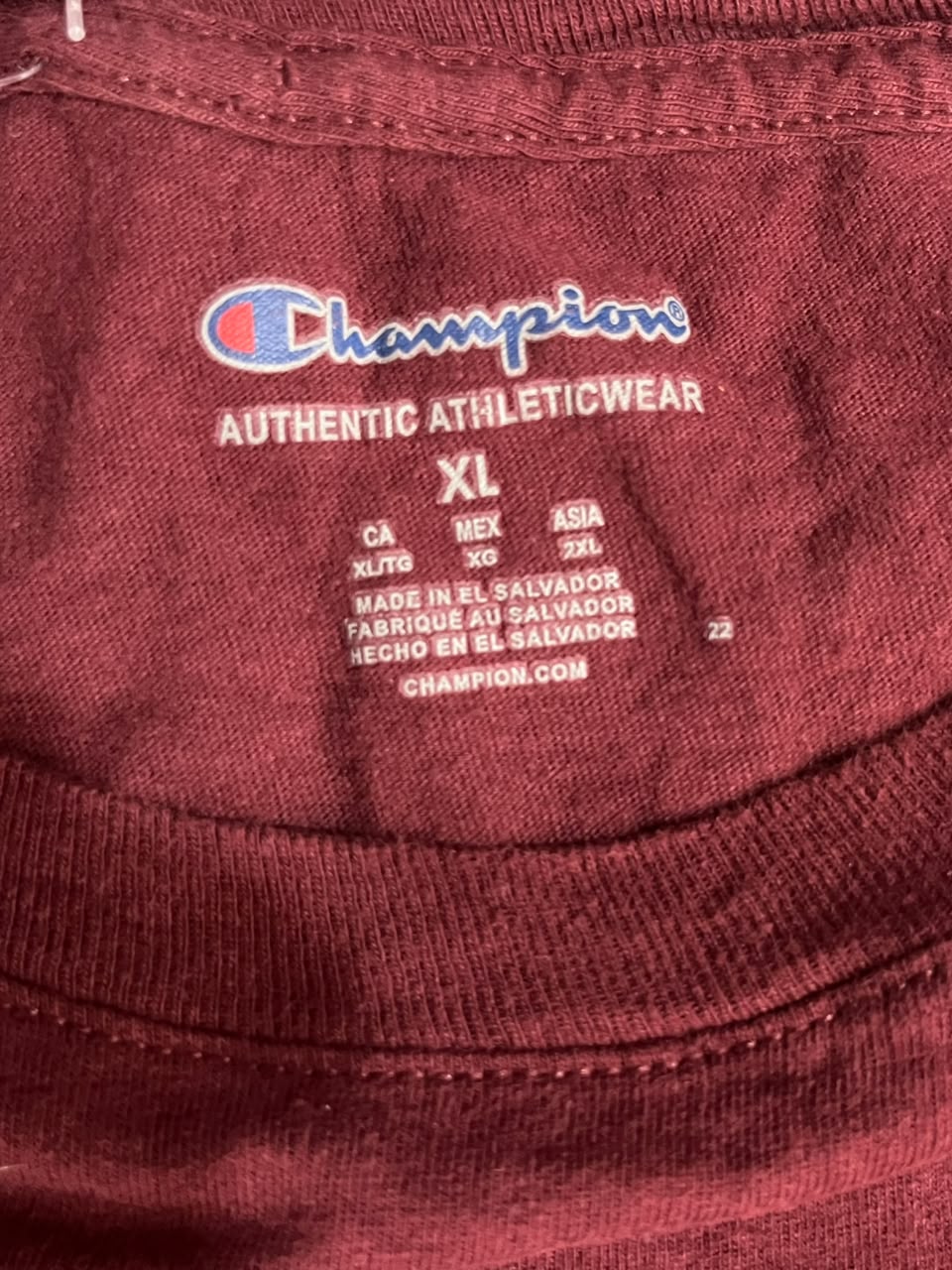 Close-up of the inside neck label of a maroon Champion athletic shirt, showing the Champion logo, 'AUTHENTIC ATHLETICWEAR', size 'XL', and country of origin text.