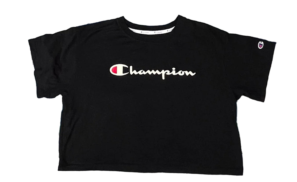 A black Champion short-sleeve crop top t-shirt with a white script logo on the chest, laid flat on a pastel tie-dye shag rug.