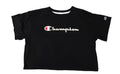A black Champion short-sleeve crop top t-shirt with a white script logo on the chest, laid flat on a pastel tie-dye shag rug.