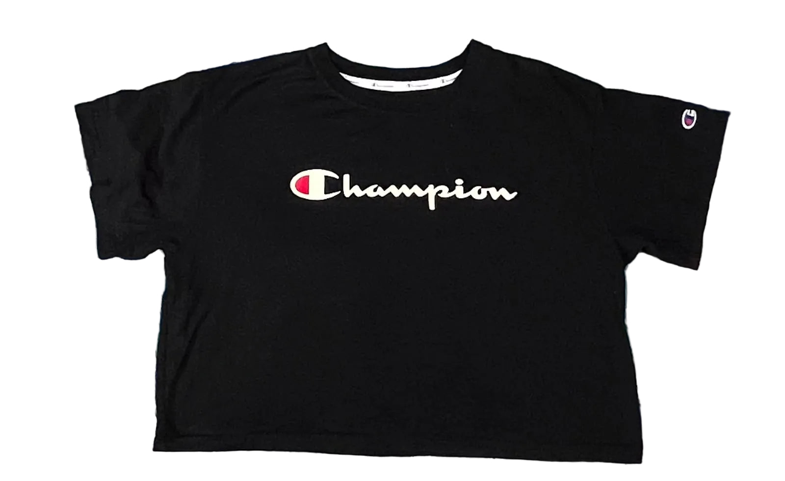 A black Champion short-sleeve crop top t-shirt with a white script logo on the chest, laid flat on a pastel tie-dye shag rug.