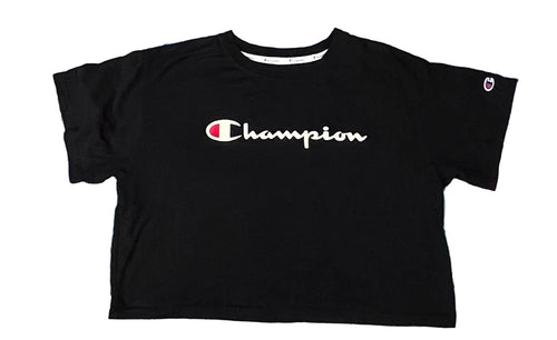 A black Champion short-sleeve crop top t-shirt with a white script logo on the chest, laid flat on a pastel tie-dye shag rug.