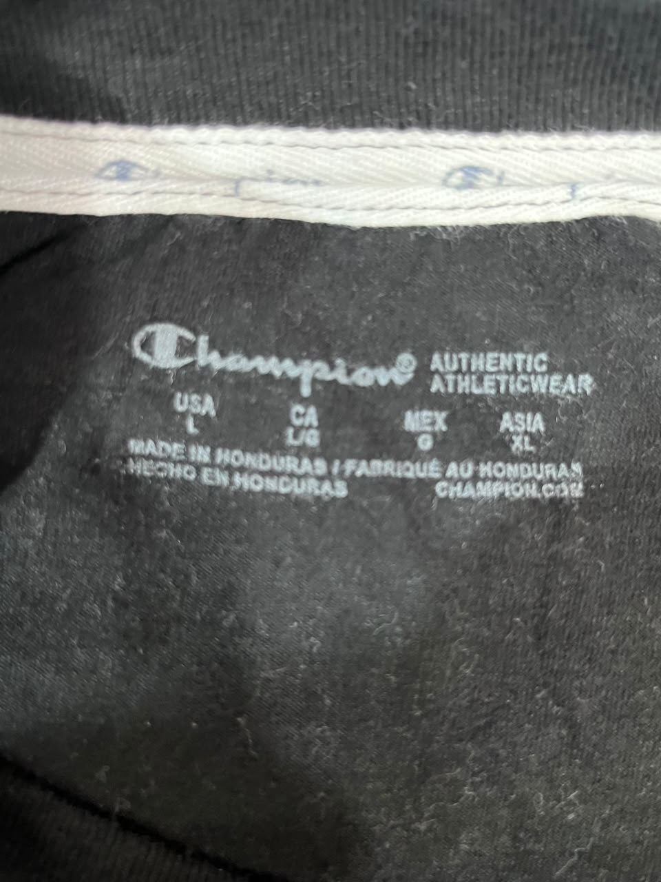 Close-up of a Champion garment interior label reading 'Authentic Athleticwear' with size and country information, on dark fabric.