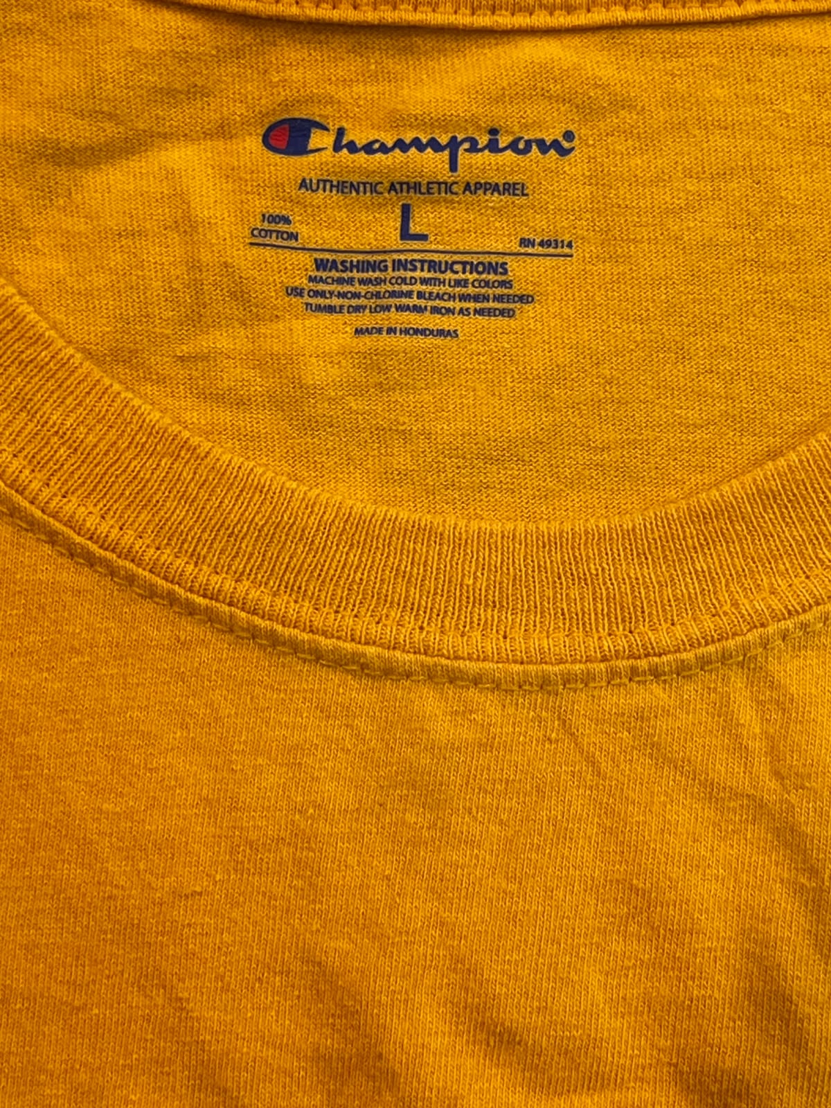 Close-up of a Champion crewneck t-shirt in a vibrant orange-yellow color, showing the inner neck label with the Champion logo and size information.