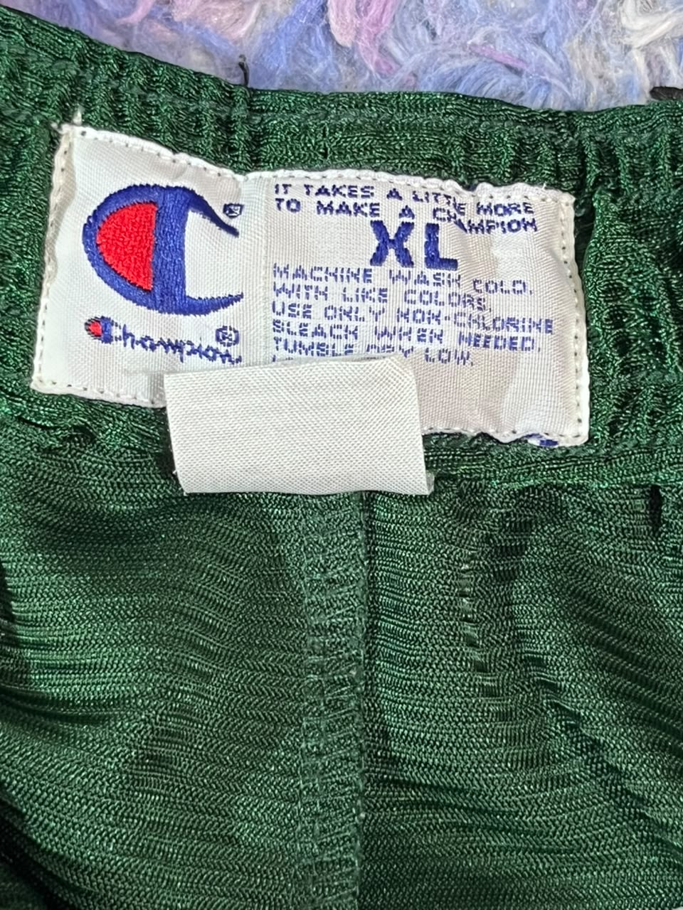 Close-up of green Champion clothing with a visible white size label showing the Champion logo and 'XL' text.