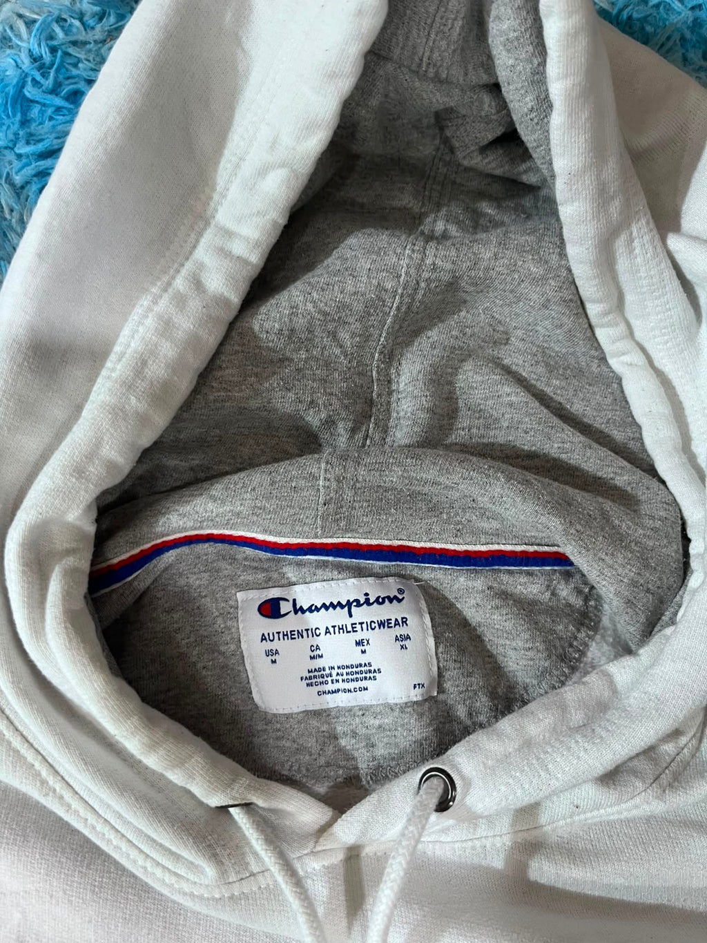 Close-up of a Champion hoodie hood interior showing the gray heather fabric, drawstring cord, and the white Champion brand label.
