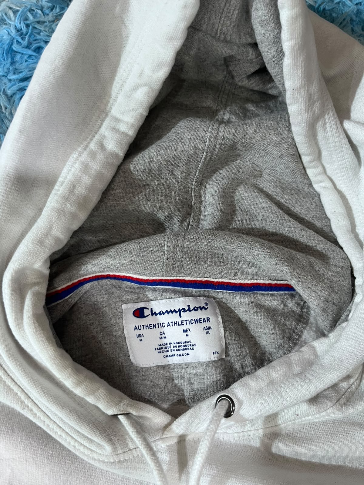 Close-up of a Champion hoodie hood interior showing the gray heather fabric, drawstring cord, and the white Champion brand label.