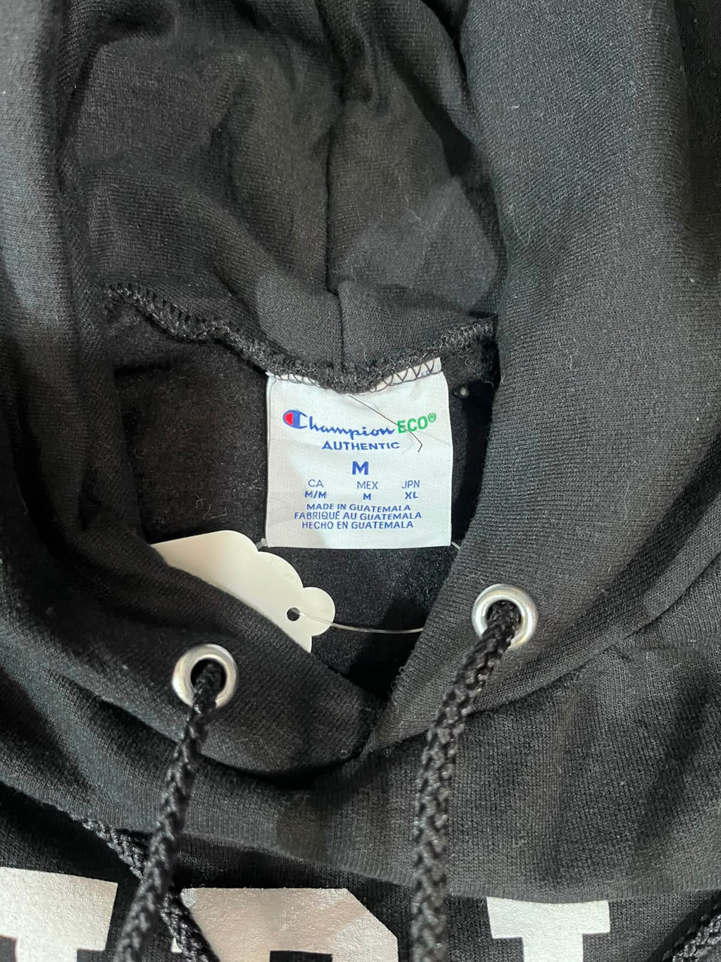 Close-up of a black Champion hoodie showing the inner neck label, drawstrings, and part of a white graphic print on the front.