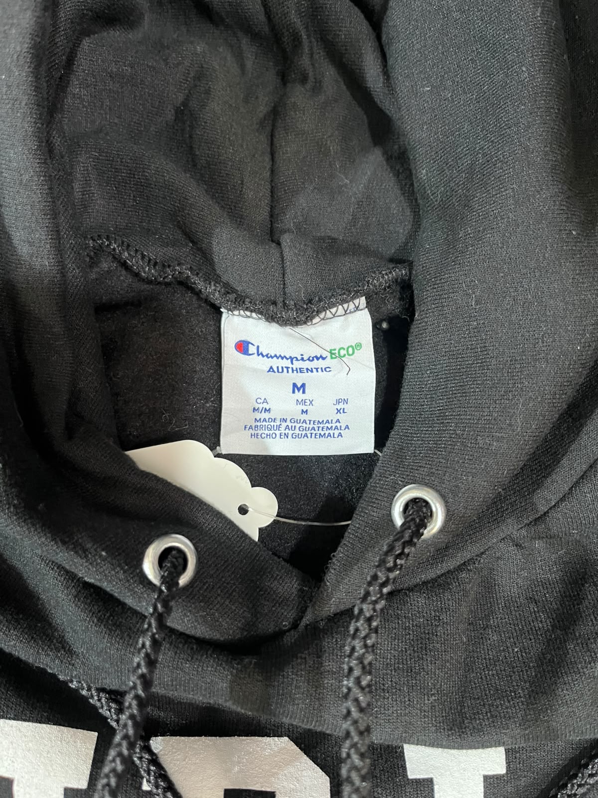 Close-up of a black Champion hoodie showing the inner neck label, drawstrings, and part of a white graphic print on the front.