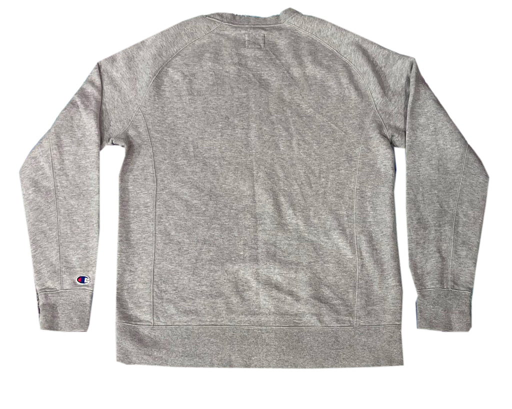 A heather gray long-sleeve crewneck sweatshirt shown from the back, featuring a small Champion logo patch on the left sleeve cuff.