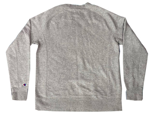 A heather gray long-sleeve crewneck sweatshirt shown from the back, featuring a small Champion logo patch on the left sleeve cuff.