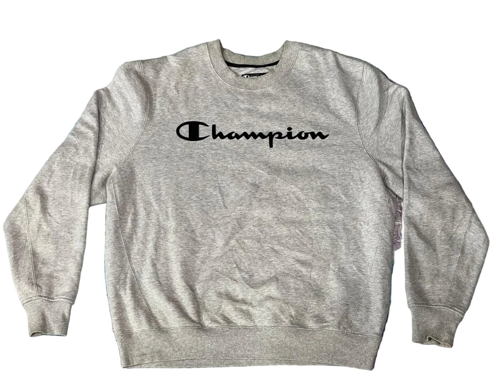 A light heather gray Champion crewneck sweatshirt with the brand name printed in black across the chest, laid flat on a textured