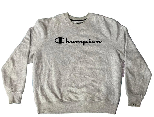 A light heather gray Champion crewneck sweatshirt with the brand name printed in black across the chest, laid flat on a textured