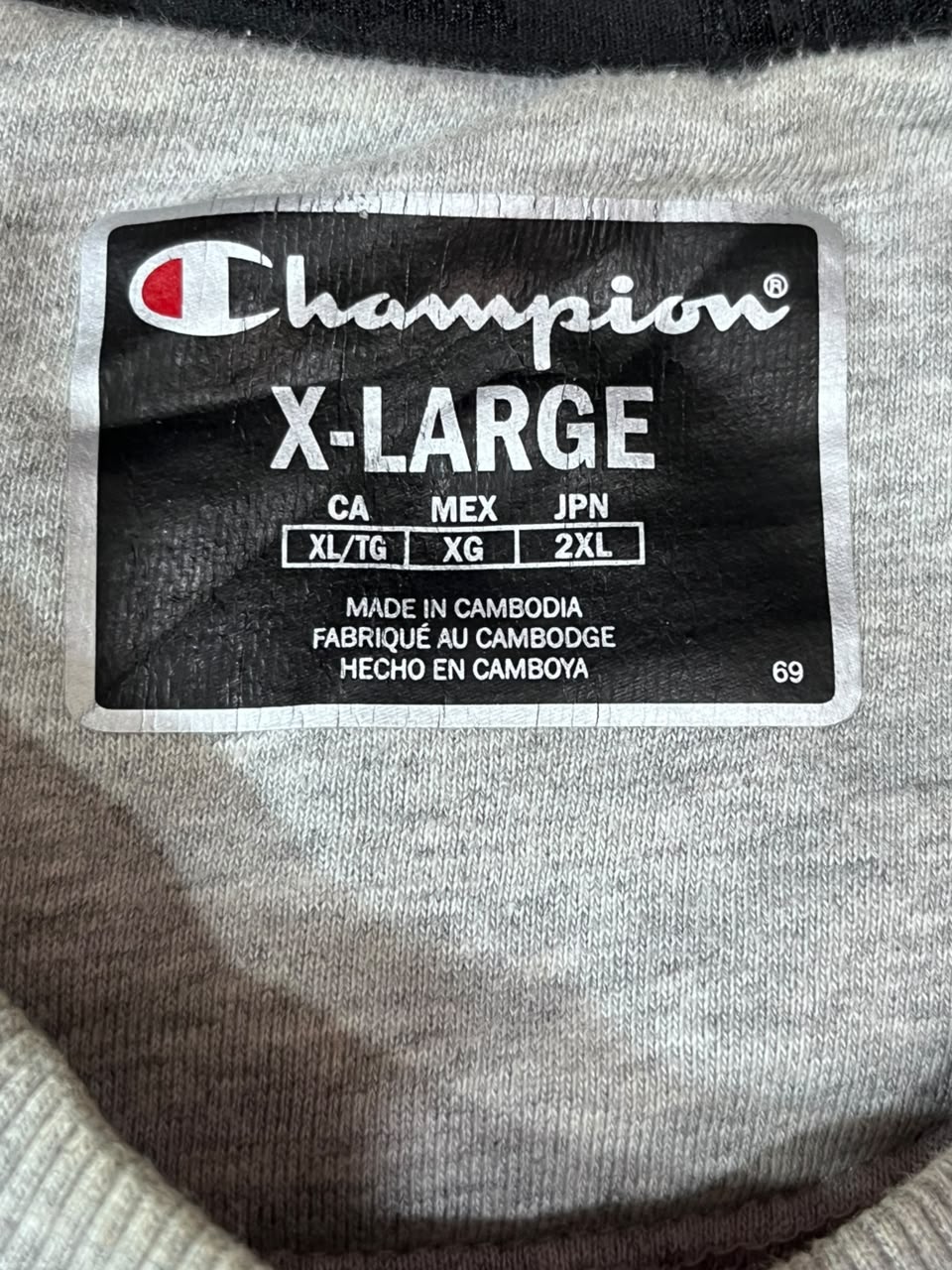 Close-up of a Champion X-Large garment label sewn onto light gray knit fabric.