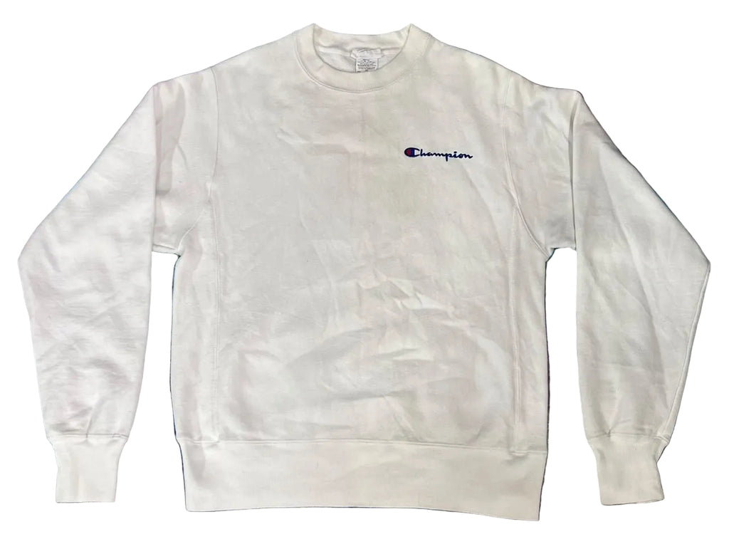 A white Champion crewneck sweatshirt with the brand's signature 'C' logo embroidered in navy blue on the left chest, laid flat on a textured blue and purple shag rug.
