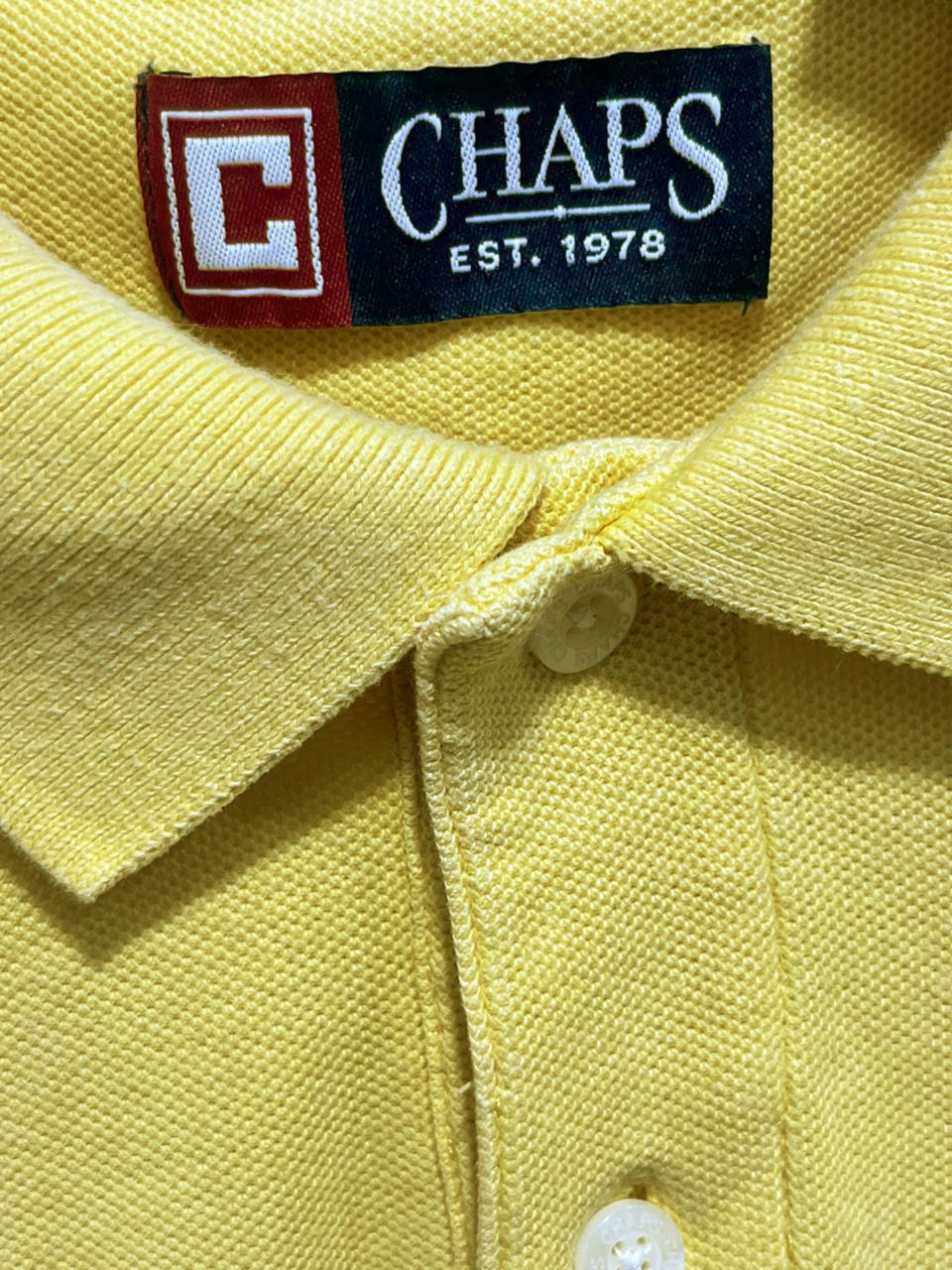 Close-up of a yellow polo shirt with a Chaps label.