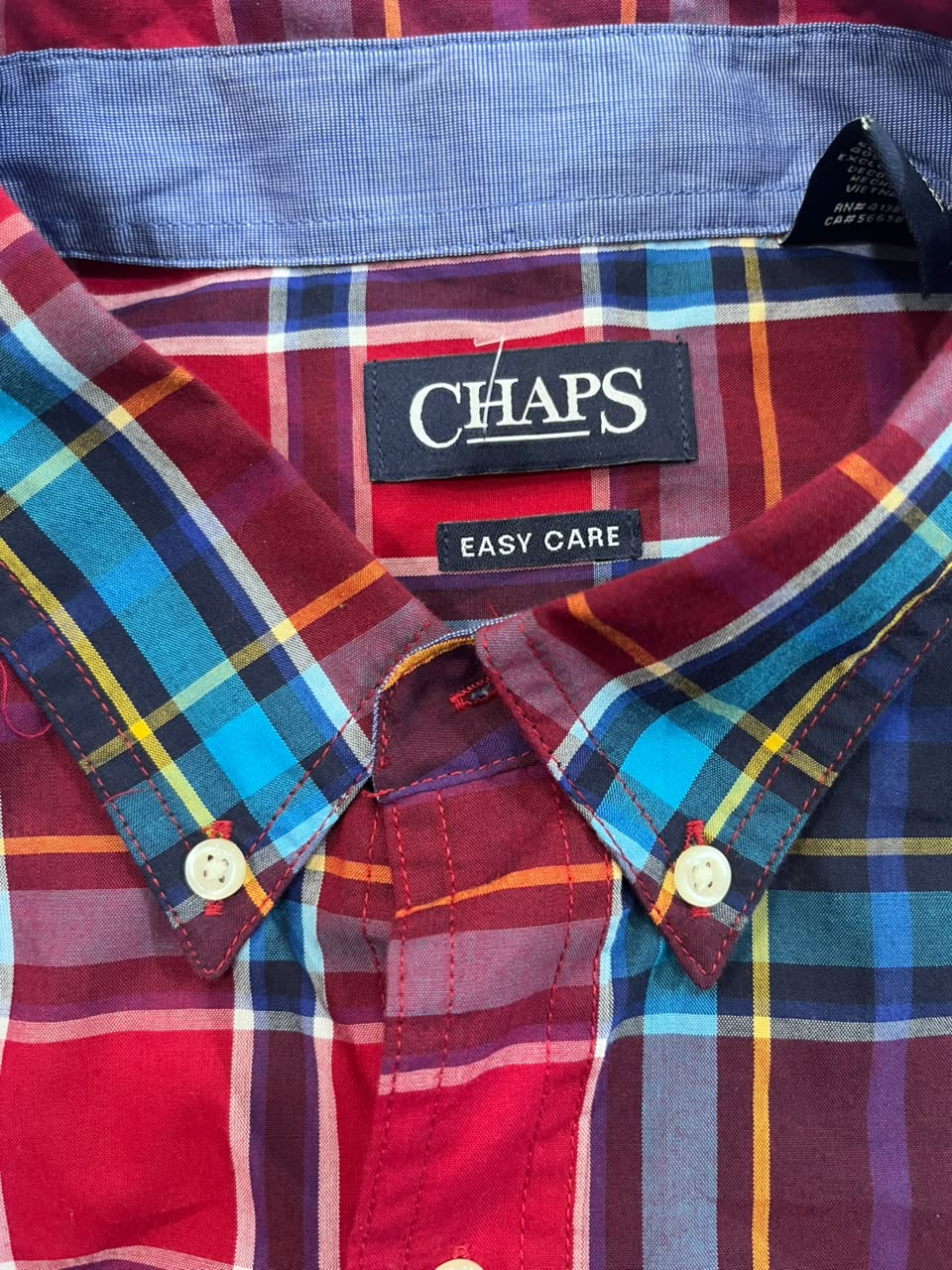 A close-up of a Chaps plaid button-down shirt collar, showing the brand label 'CHAPS' and 'EASY CARE' on a red, blue, and yellow tartan pattern.