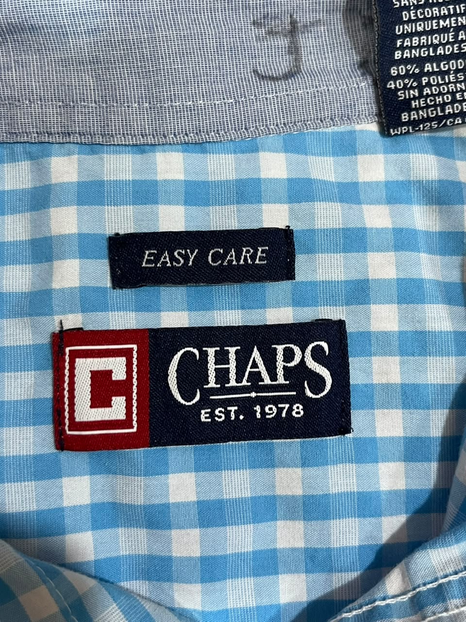 Close-up of a blue and white gingham shirt showing the brand label 'CHAPS EST. 1978' and an 'EASY CARE' tag on the inside collar.