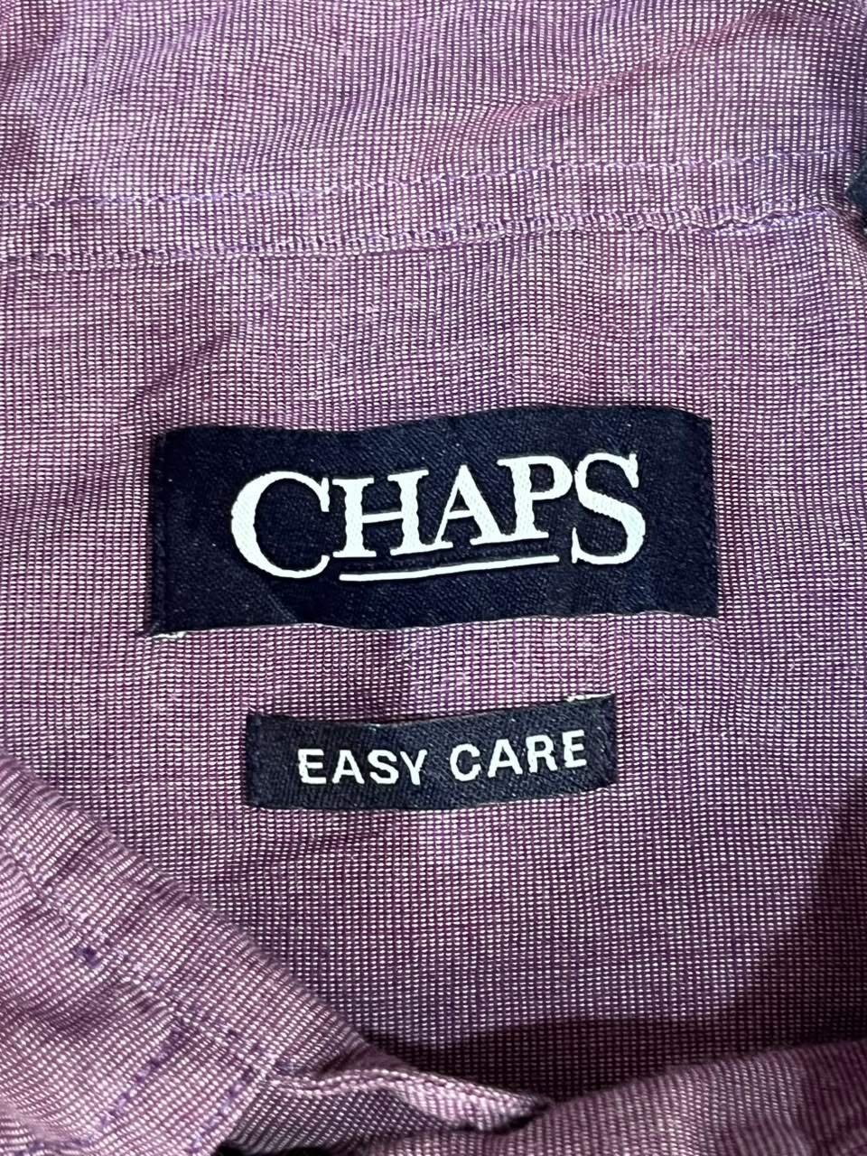 Close-up of a purple textured fabric garment showing two brand labels: a black CHAPS label with white text and a smaller black EASY CARE label below it.