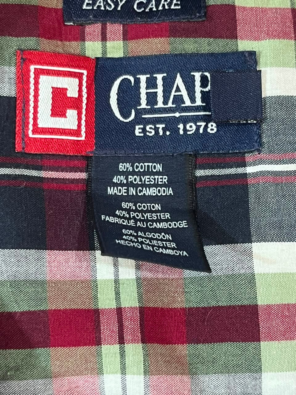 Close-up of a CHAP plaid shirt label and inner neck area, showing the brand name 'CHAP EST. 1978', a red-and-white 'C' logo patch, and a black care tag with cotton and polyester composition details.