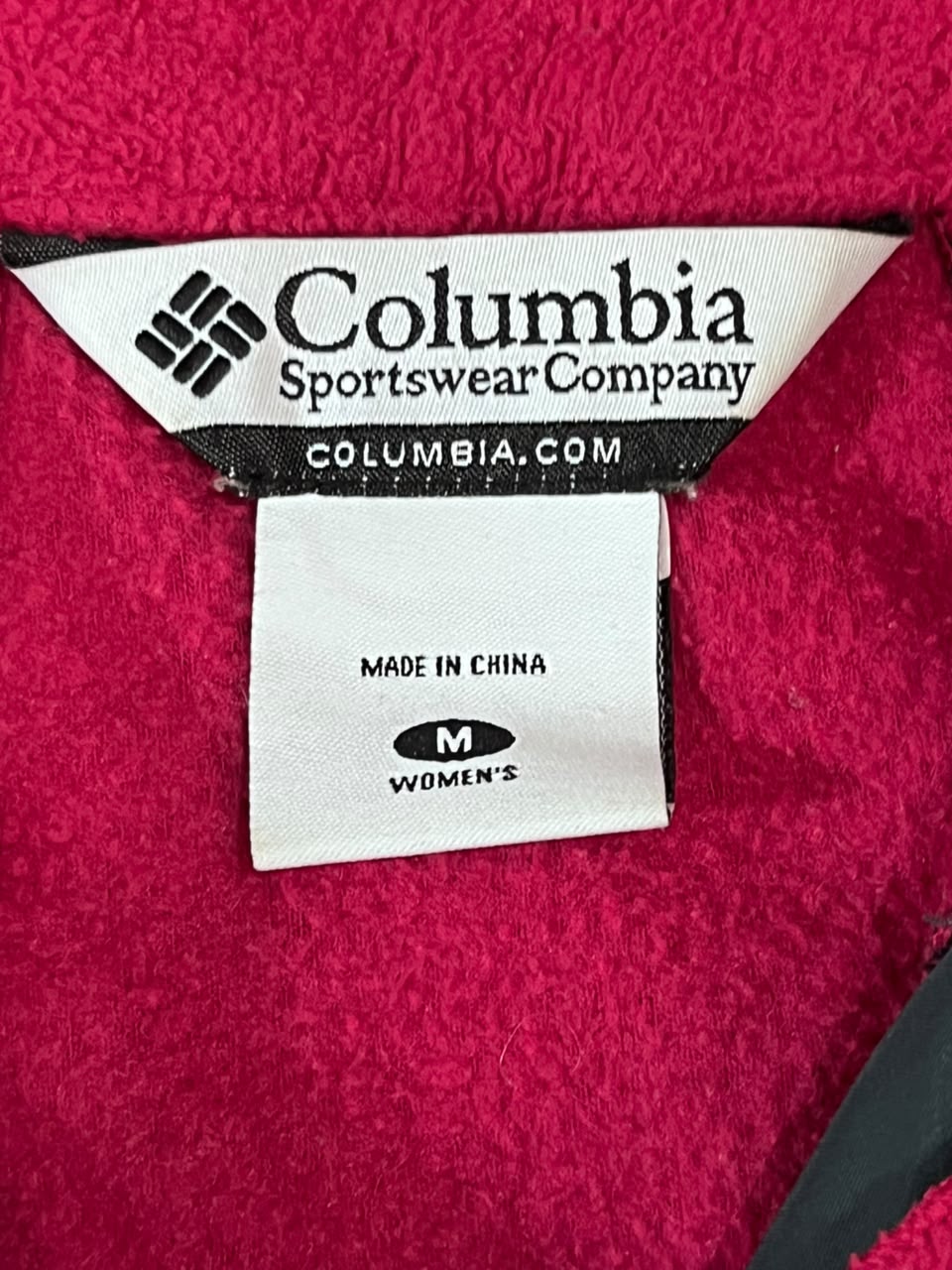 Close-up of a Columbia Sportswear Company garment label on a bright pink fleece or plush fabric, with size information reading M Women's.