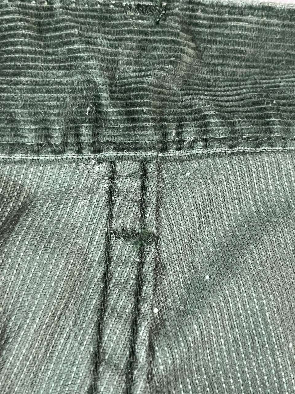 Close-up of dark gray ribbed fabric with a horizontal seam and vertical stitching, showing a textured material detail.