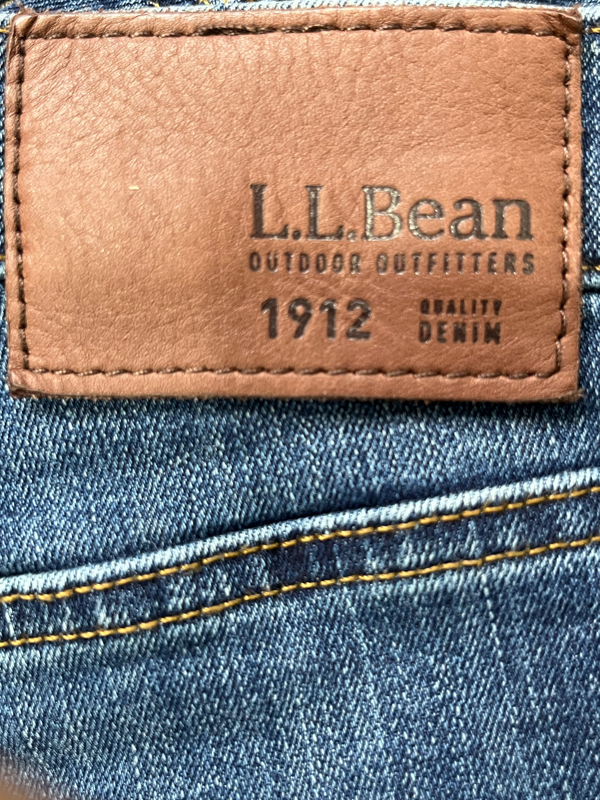 Close-up of a blue denim jeans back pocket showing a tan leather patch with the embossed brand name 'L.L.