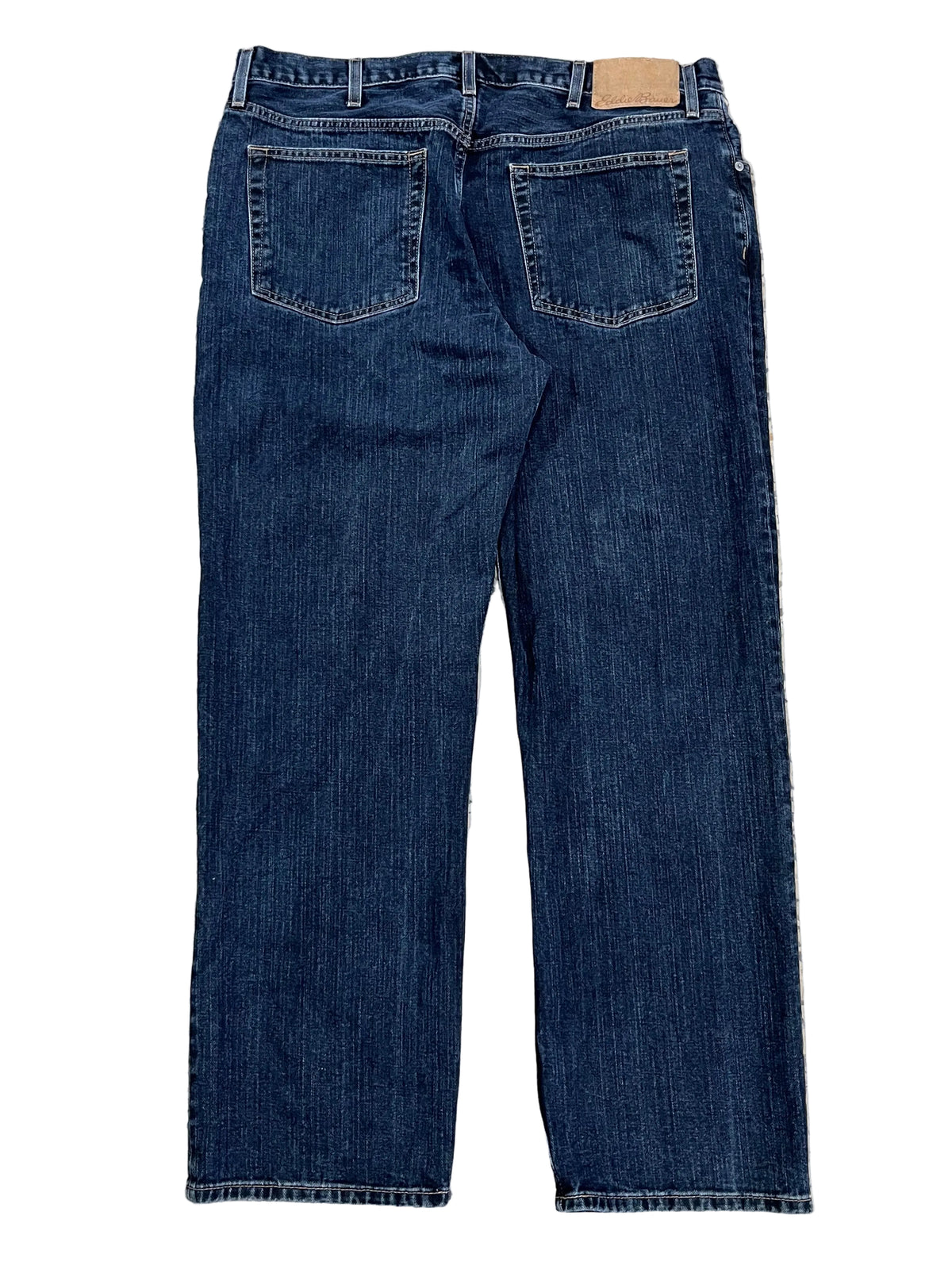 Back view of dark blue denim jeansshowing the waistband, belt loops, back pockets, and hem.