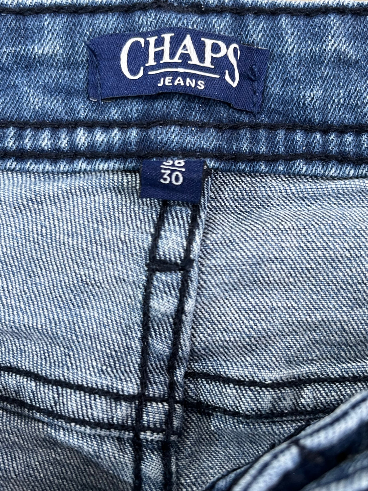 Close-up of a pair of blue denim jeans showing the waistband, brand label reading CHAPS JEANS, size tag 28 30, and detailed stitching.
