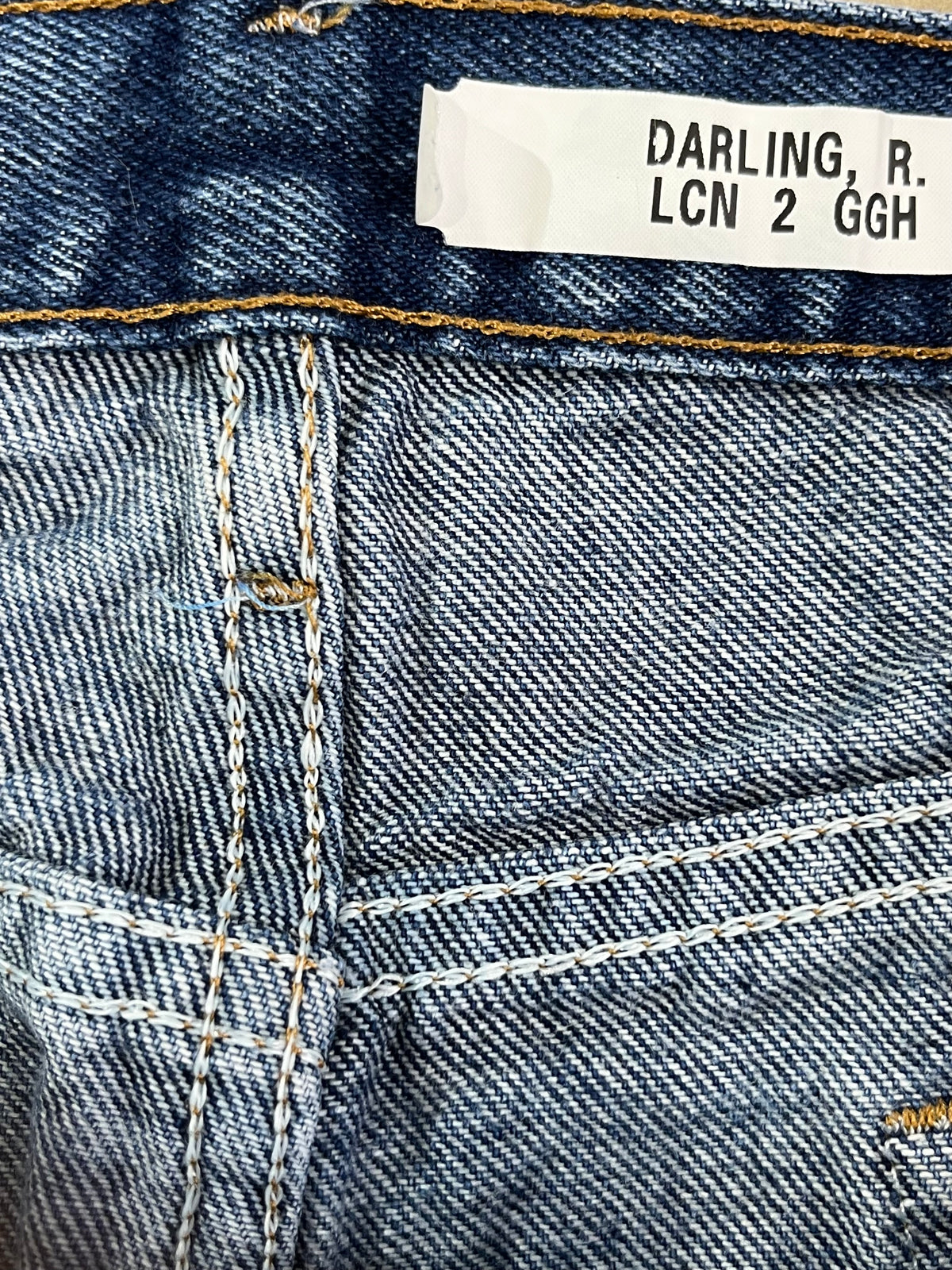 Close-up of blue denim jeans showing the waistband, white size label reading 'DARLING, R. LCN 2 GGH', and detailed stitching.