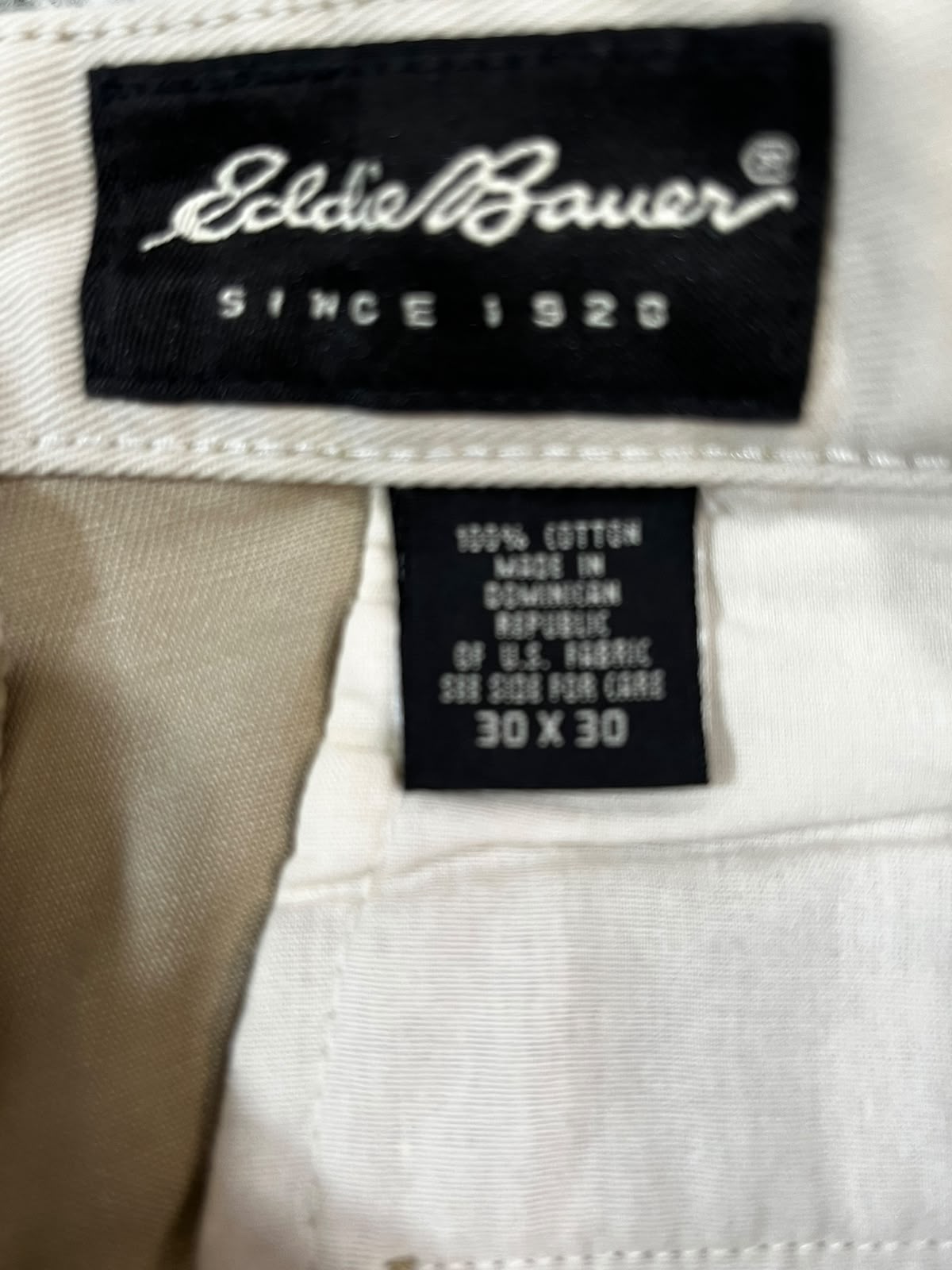 Close-up of a garment's inner neck label area showing an Eddie Bauer brand tag and a size tag on off-white fabric.