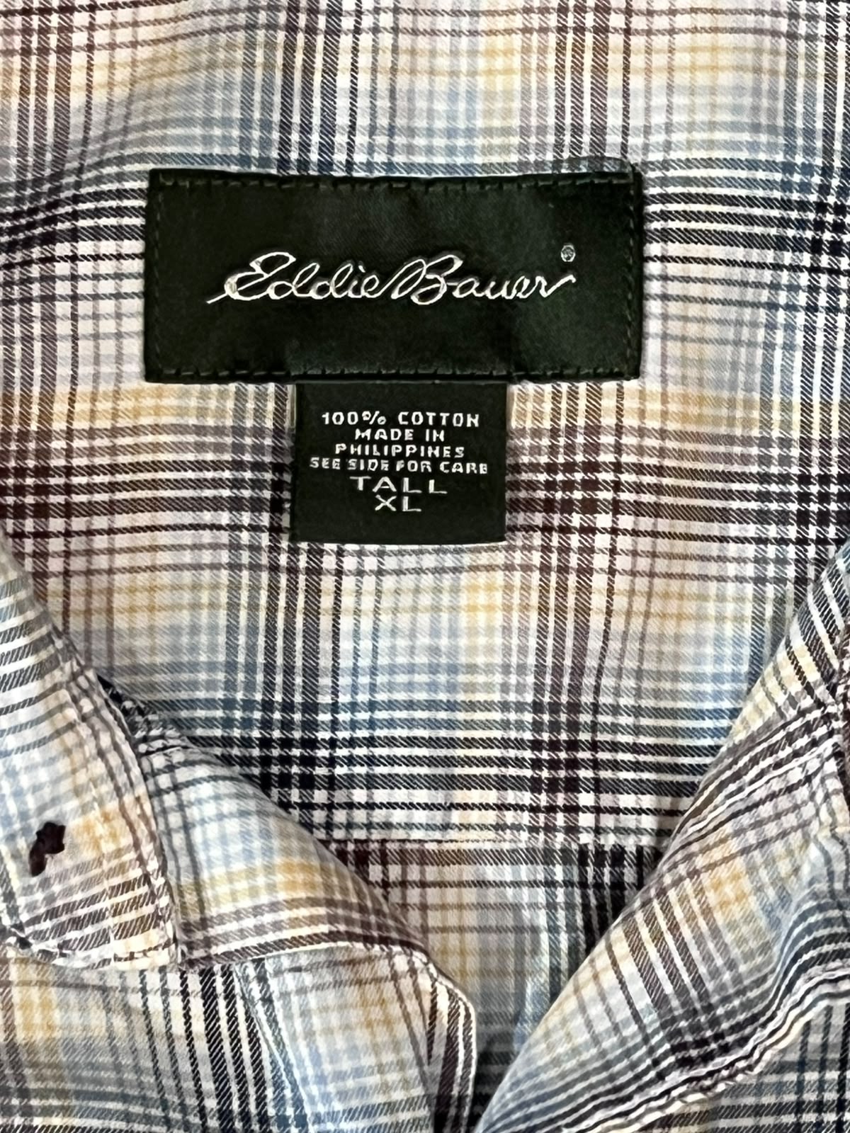 Close-up of a plaid button-down shirt collar with a black Eddie Bauer brand label visible inside the neck.