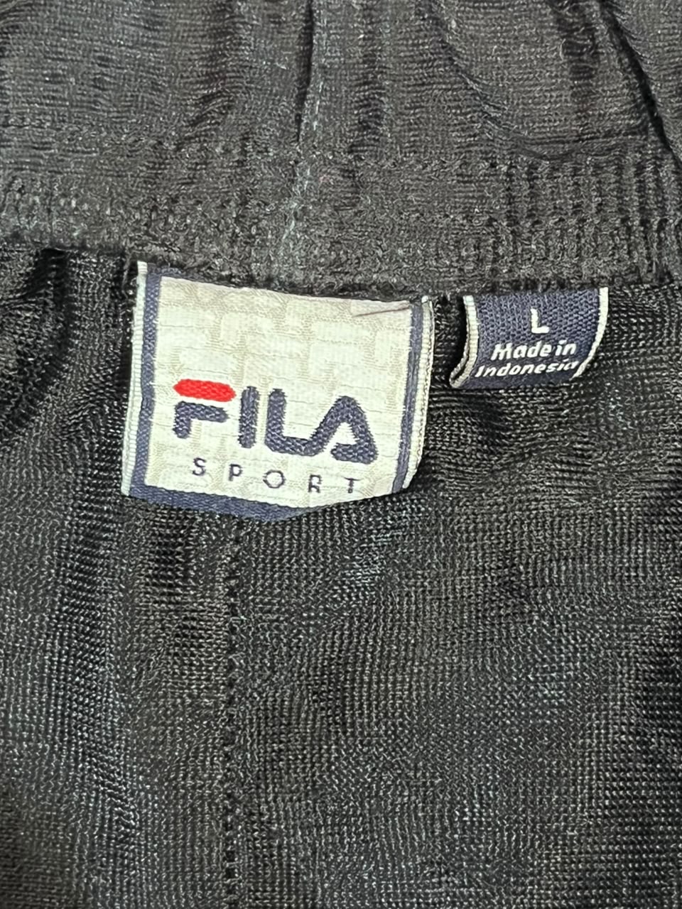 Close-up of a black ribbed waistband with a FILA SPORT brand label and a small 'Made in Indonesia' tag.