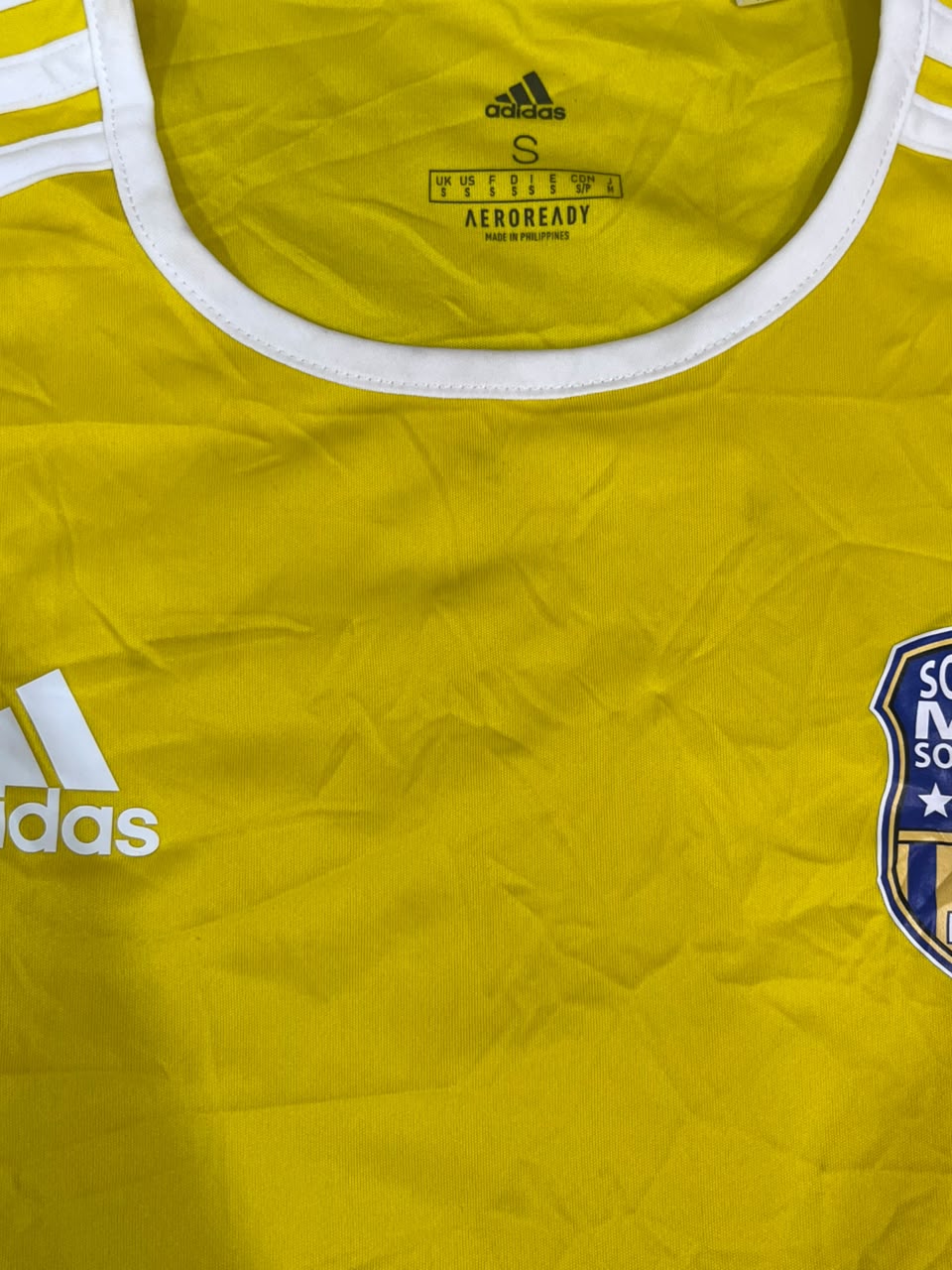 Close-up of a yellow Adidas soccer jersey with white trim at the collar, white Adidas logo on the chest, and part of a San Diego N. Stars crest visible on the right side.
