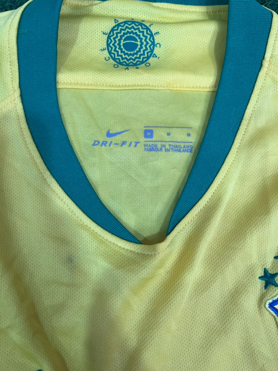 Close-up of a yellow soccer jersey with a blue V-neck trim, showing the Nike Dri-FIT branding and a circular emblem inside the collar.
